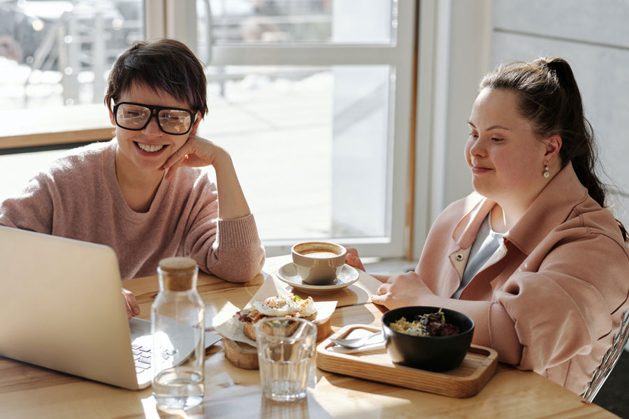 Deux jeunes femmes d’affaires assises à une table en regardant un ordinateur portative tout en ayant un repas