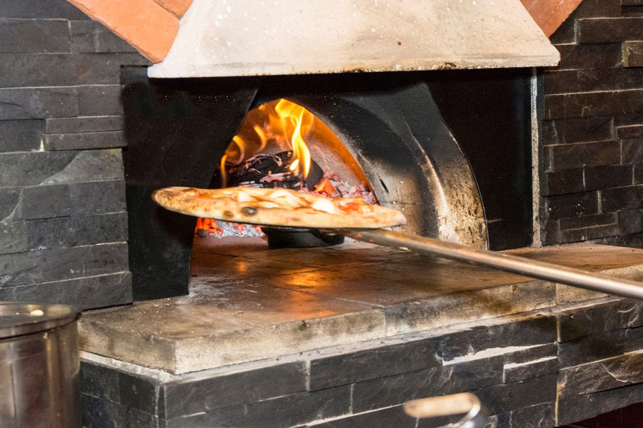Pizza on a board being taken out of a wood fired oven